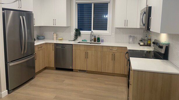 A modern kitchen with stainless steel appliances, wooden cabinets, and a herringbone tile backsplash. - Cozy quiet place 15 min driver to airport perfect place for family and friends. (Calgary)