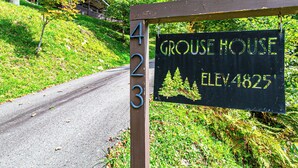 Señal de Grouse House, con una altitud de 4825, ubicada al lado de una carretera con un área verde y árboles de fondo.