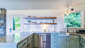 Una cocina con armarios azul claro, un lavavajillas de acero inoxidable y una ventana con vistas al verdor.