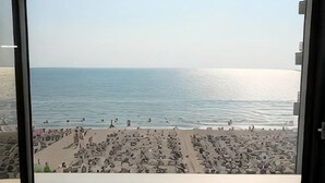 Vista desde una ventana hacia una playa con gente y cielo despejado.
