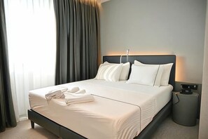 A neatly made bed with pillows and a folded towel, a bedside table with a lamp, and a window with curtains. - Adria Palace (Durres)