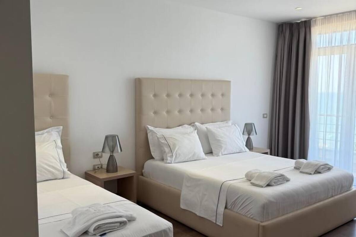 Une chambre d’hôtel avec deux lits, une grande fenêtre avec des rideaux et une décoration aux couleurs neutres.