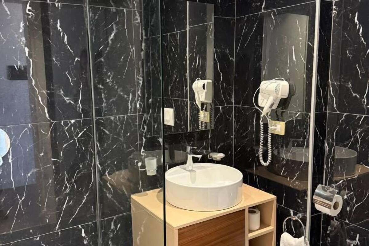Une salle de bain avec un mur en marbre, un lavabo rond, un miroir, un porte-serviettes et un porte-rouleau de papier toilette.