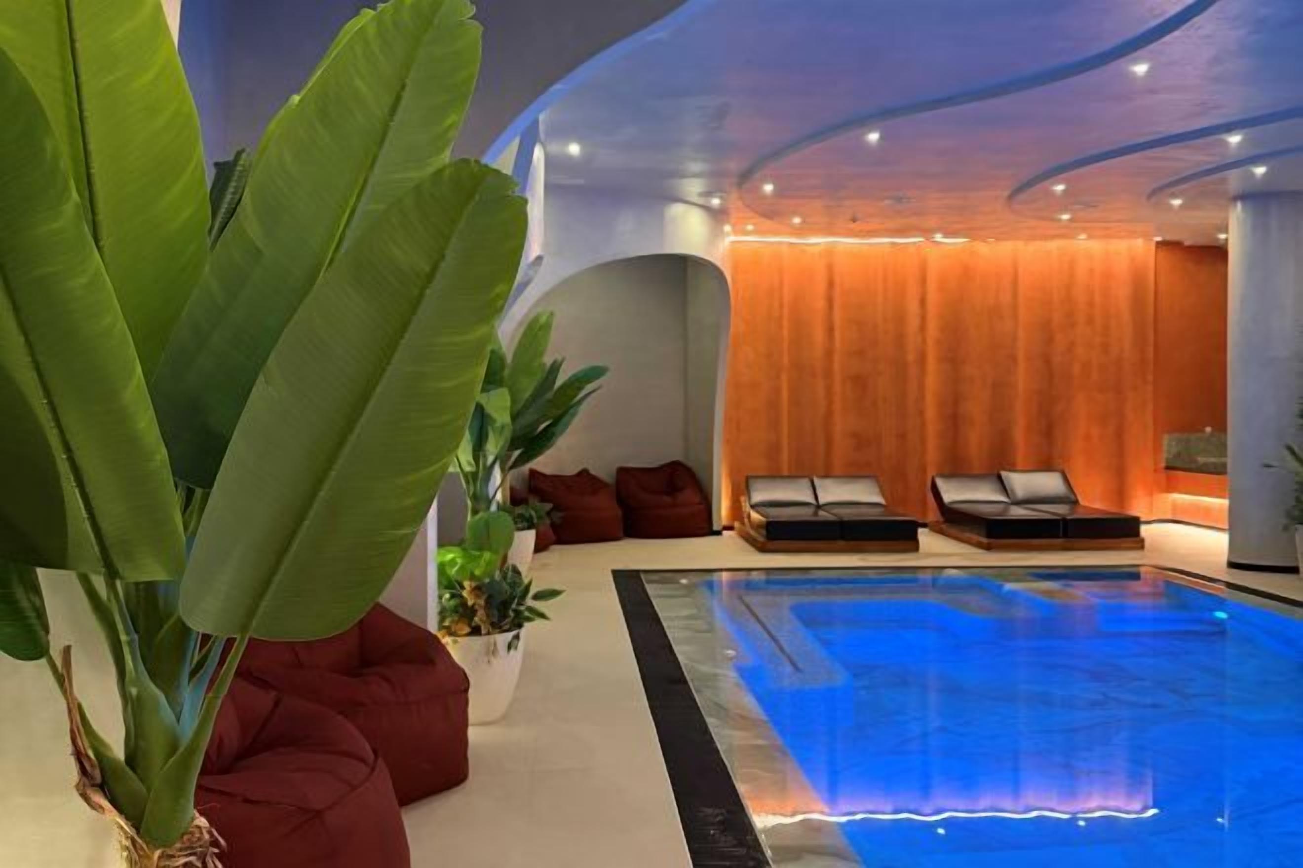 A modern indoor swimming pool area with lounge chairs and potted plants.