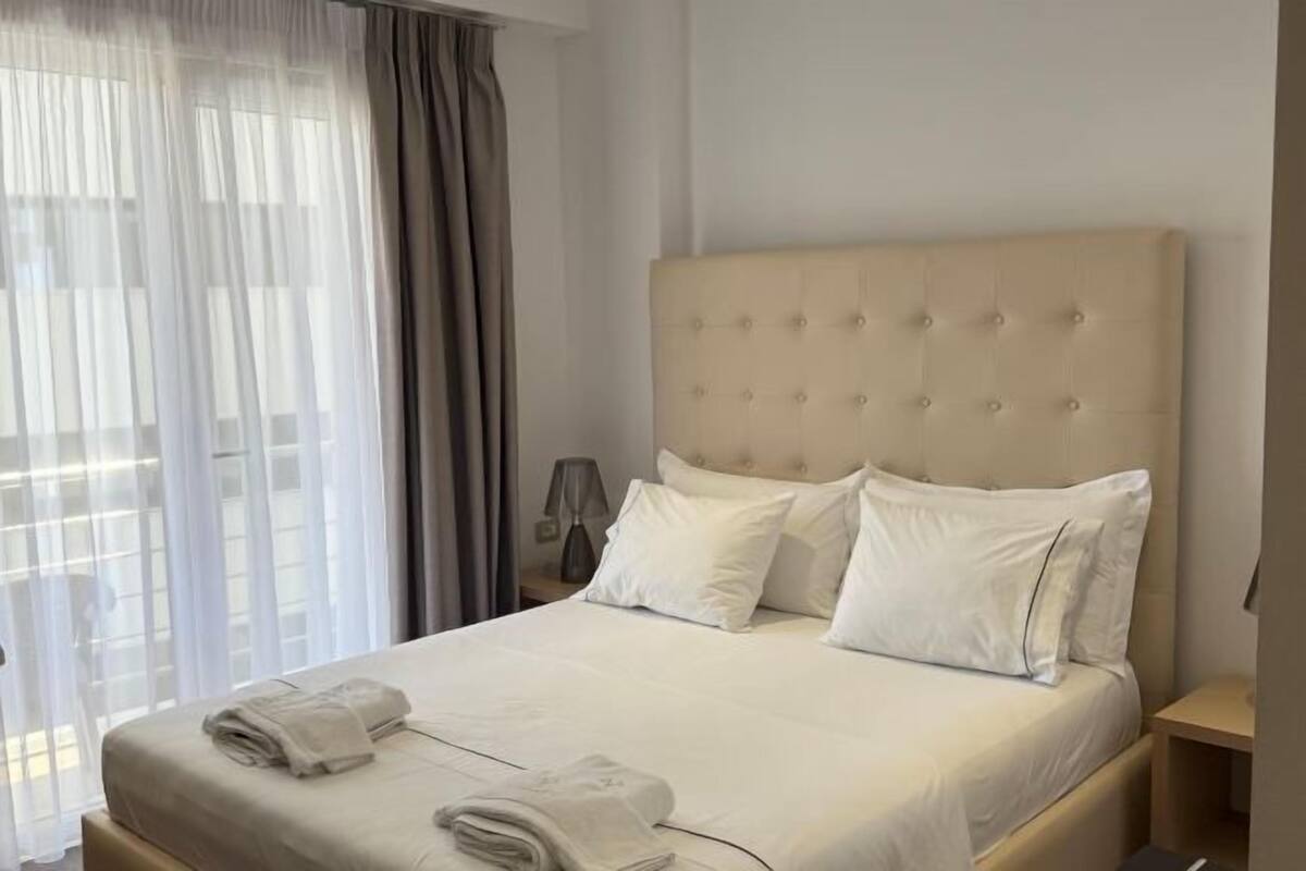 Une chambre d’hôtel avec un grand lit, deux tables de chevet, une lampe et des rideaux légers.