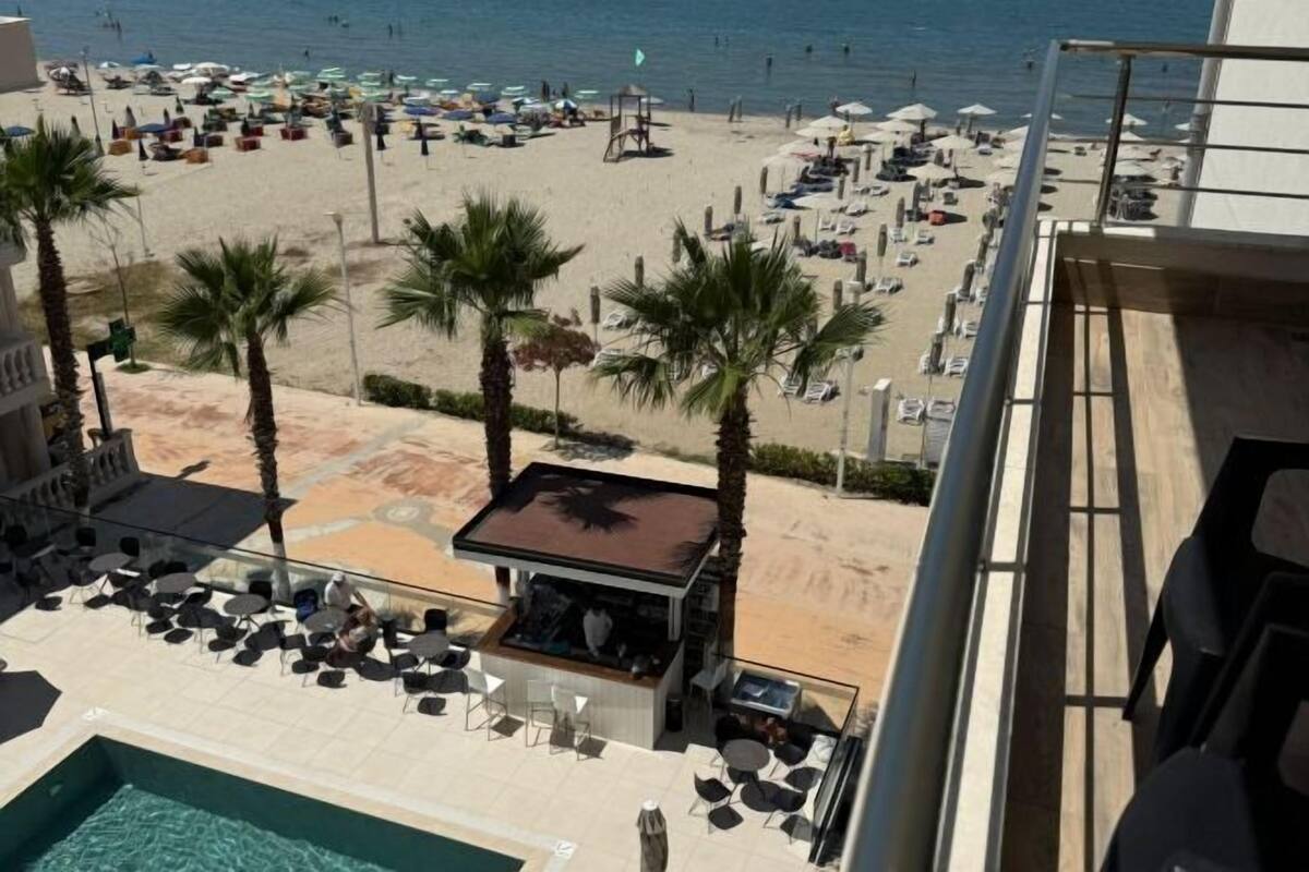 Un hôtel doté d’une piscine, offrant une vue sur la plage, bordé de palmiers et disposant d’un espace extérieur aménagé pour s’asseoir.