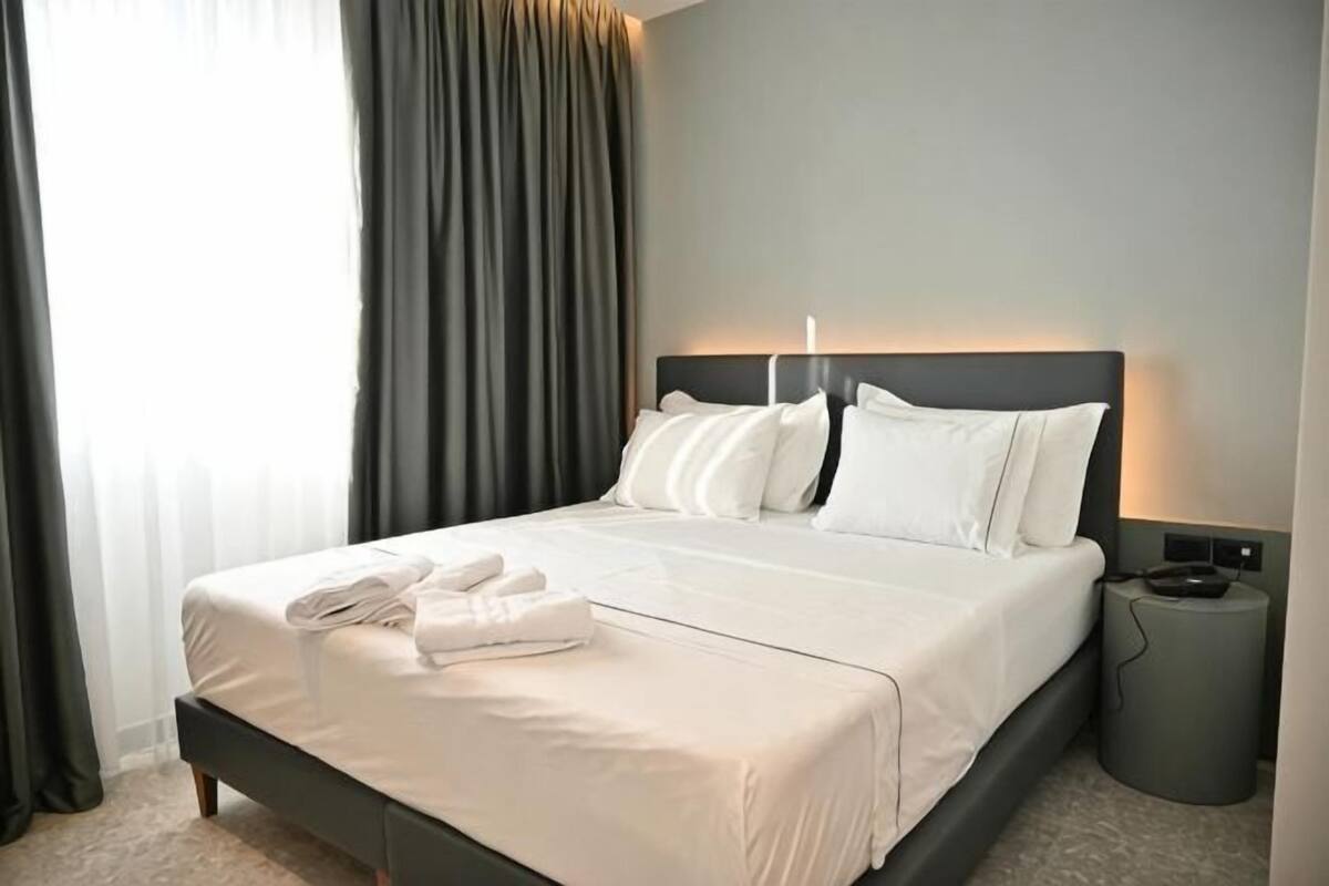 Un lit bien fait, avec du linge de lit et des serviettes blanches, une tête de lit moderne et une table de chevet avec une lampe.