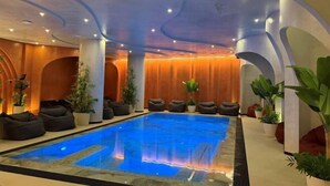 Una piscina interior con un elemento acuático azul, rodeada de zonas de estar y plantas en macetas.