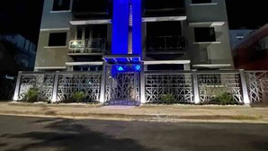 Un edificio de varios pisos con una estructura central iluminada en azul, posiblemente una escalera o ascensor, rodeada por una cerca de metal.