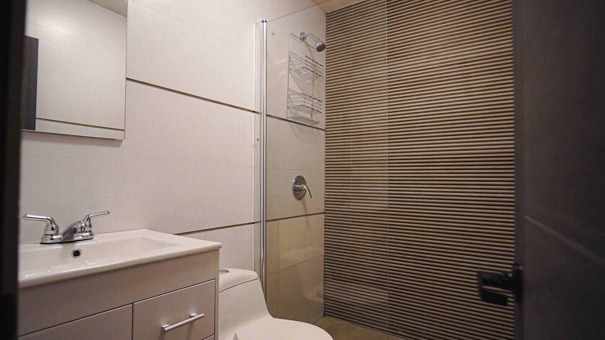 A bathroom with a white sink, mirror, and toilet. There is a shower area with a glass door and a towel rack.