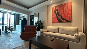 Sala de estar moderna com sofá, mesa de centro e uma poltrona. Há uma janela grande que oferece luz natural e vista para o exterior.
