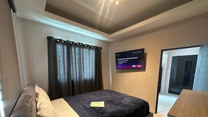 Quarto com cama, televisão fixada na parede e escrivaninha.