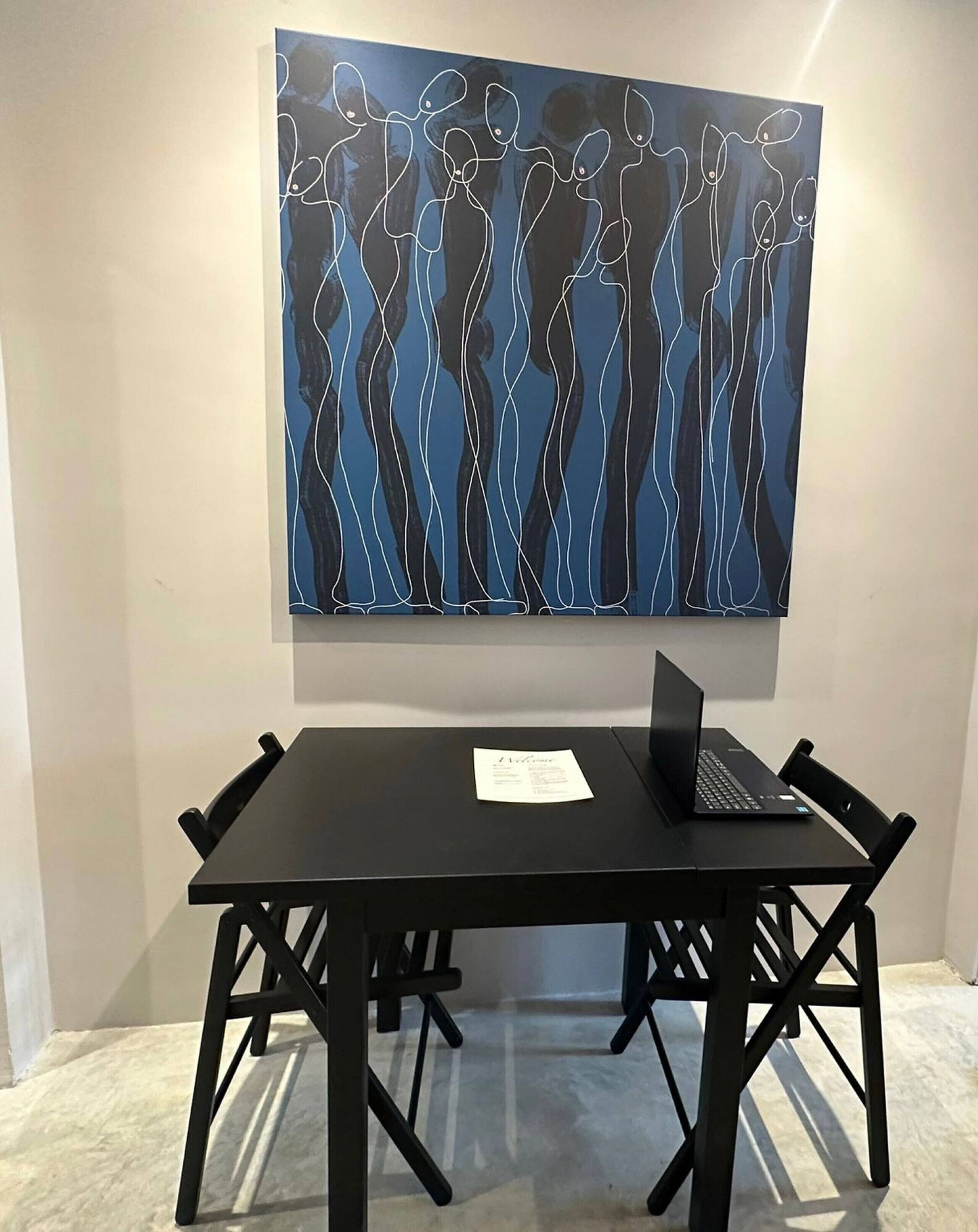 A room with a black table and chairs, a laptop, and a large abstract painting on the wall.
