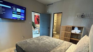 A modern hotel room with a large bed, a TV mounted on the wall displaying streaming services, a wooden wardrobe, and a bathroom visible through an open door. - 4 bedroom 3 bathroom apt E (San Juan)