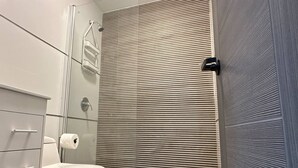A modern bathroom with a toilet, a shower enclosure, and a towel rack. - 4 bedroom 3 bathroom apt E (San Juan)