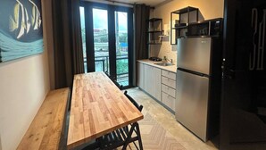 A modern kitchen with a wooden dining table, a refrigerator, and a view of a cityscape through large windows. - 4 bedroom 3 bathroom apt E (San Juan)