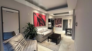A modern living room with a sofa, coffee table, and a large plant. There are abstract paintings on the walls and a door in the background. - 4 bedroom 3 bathroom apt E (San Juan)