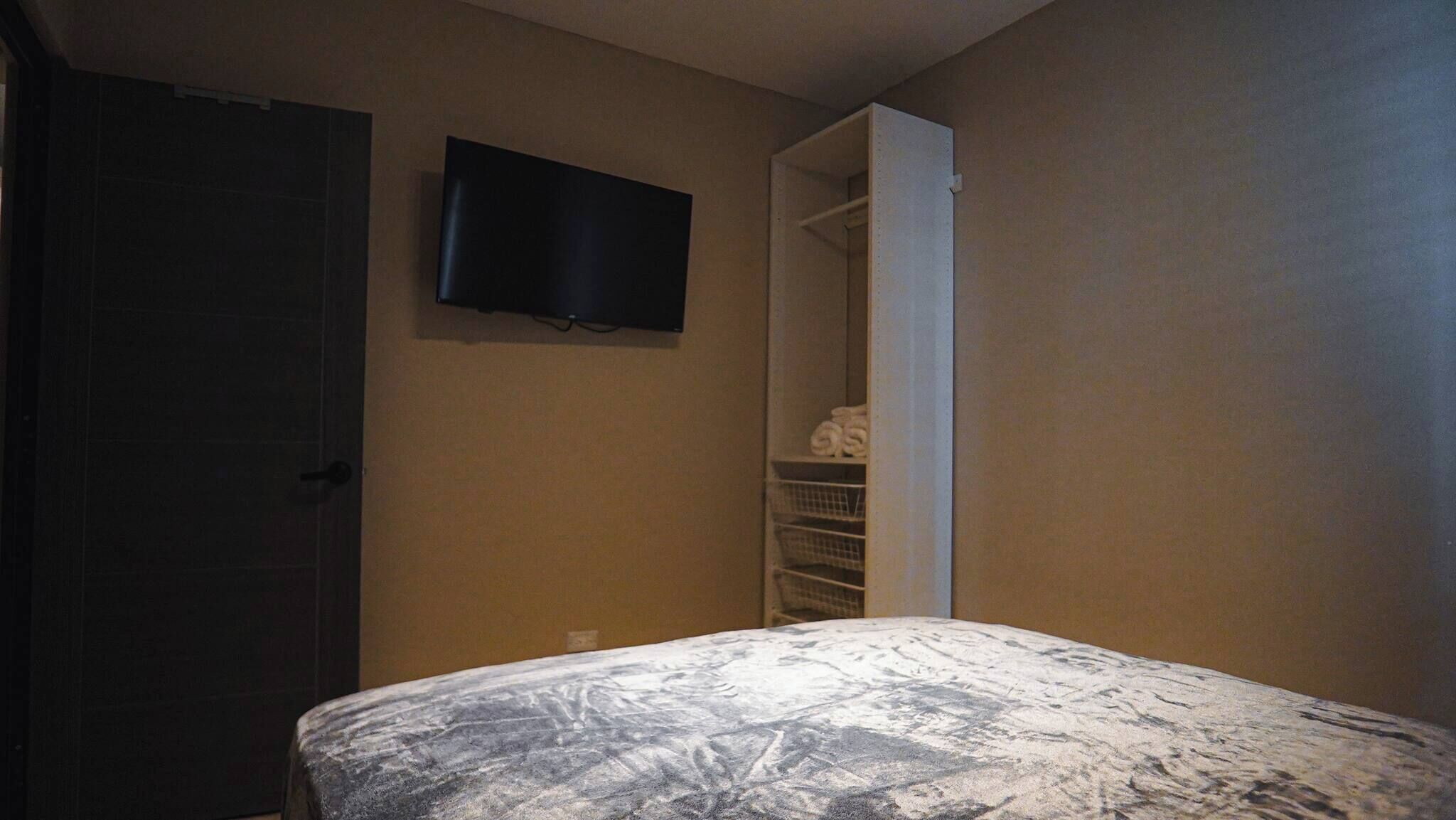 A bedroom with a bed, a wardrobe, and a television on the wall.