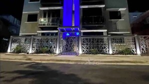 A multi-story building with a central blue-lit structure, possibly a staircase or elevator, surrounded by a gated entrance with metal fencing. - Dream apt: 8BD, 6BA, parking. (San Juan)