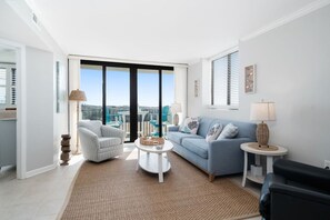 Ein modernes Wohnzimmer mit Sofa, Sessel, Couchtisch und Blick auf die Stadt durch große Fenster.