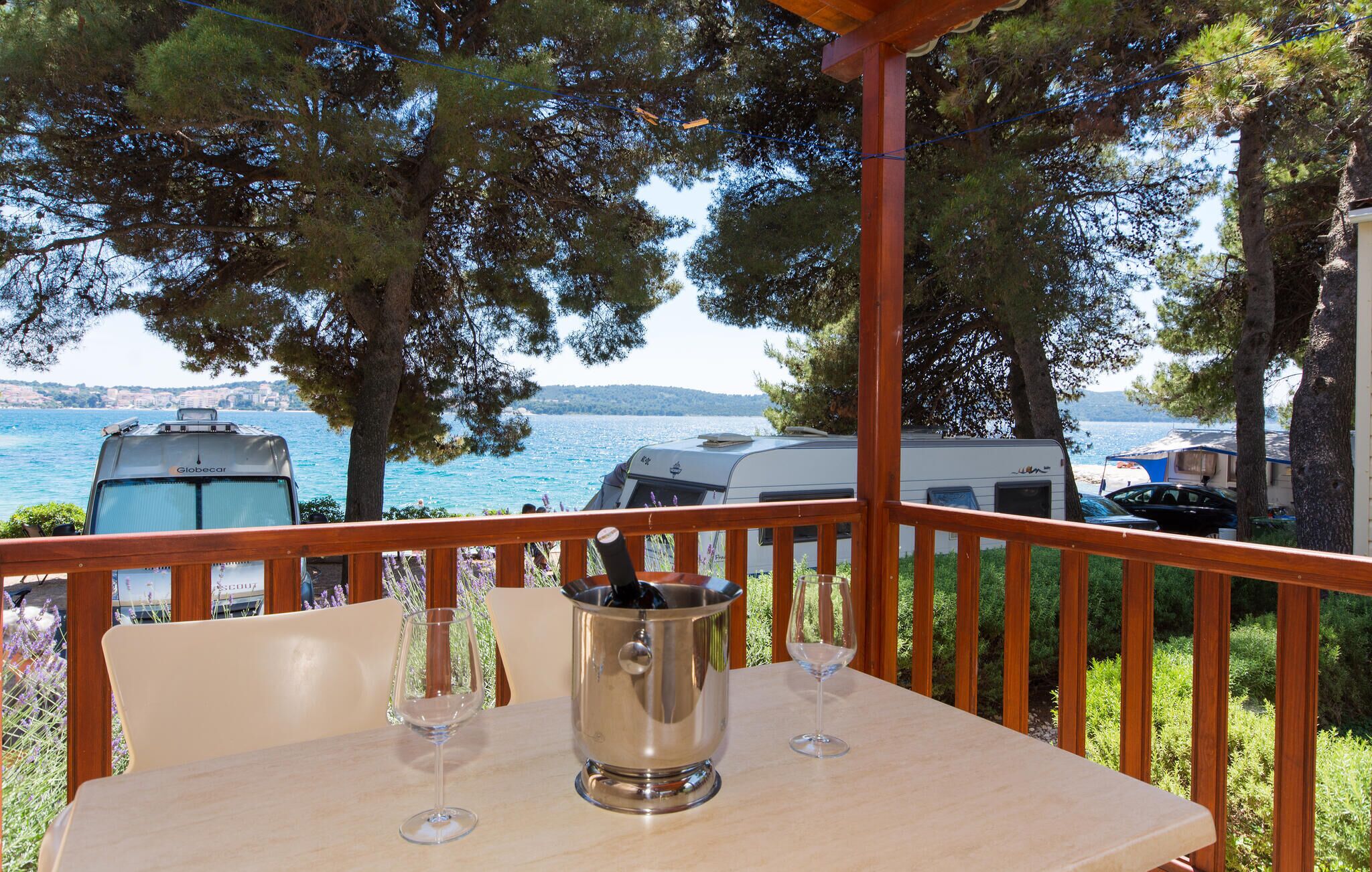 A table with two wine glasses and a metal container, overlooking a lake with RVs parked nearby.
