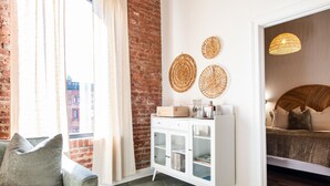 Um quarto com parede de tijolos, um armário branco com portas de vidro, uma cama com cabeceira de madeira e um pendente de luz trançado.