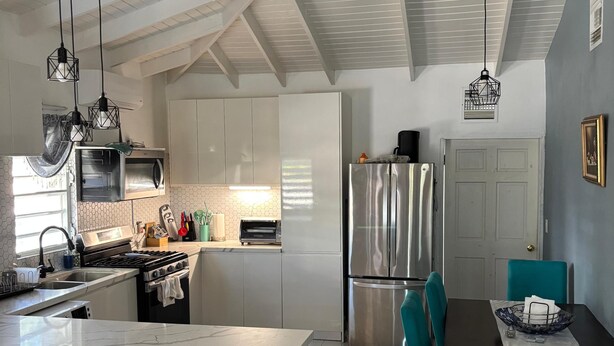 Een moderne keuken met een centraal eiland, roestvrijstalen apparatuur en teal-kleurige stoelen rond een eettafel.