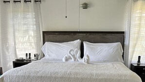 Een net opgemaakt bed met een witte quilt en twee zwaan-vormige kussens, een houten hoofdbord en een marmeren vloer.