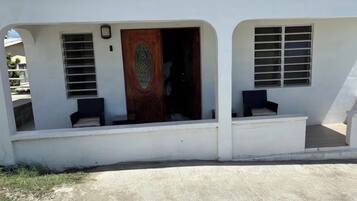 A building with a white exterior, a wooden door, and two windows with shutters.