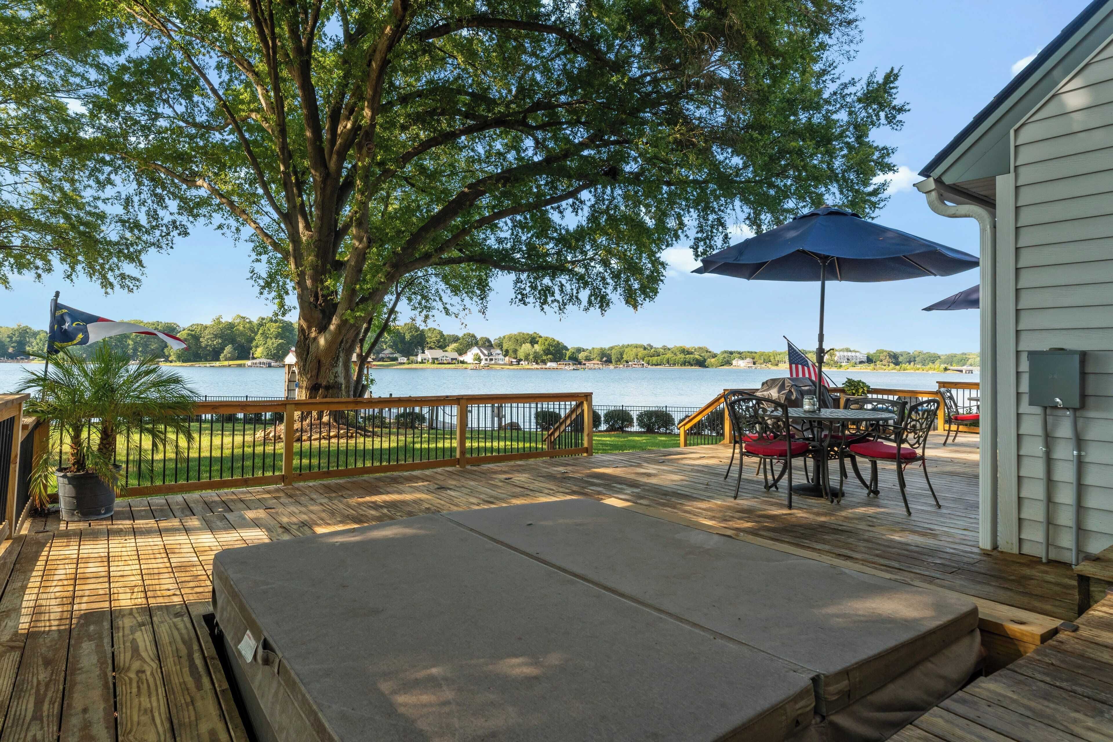 A deck with a table and chairs, overlooking a lake with a view of a bridge and buildings in the distance.