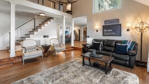 A spacious living room with a staircase, a fireplace, and a large window. - Lakefront Home w/ Game Room & Hot Tub Ponderosa Peninsula by Avantstay (Mooresville)