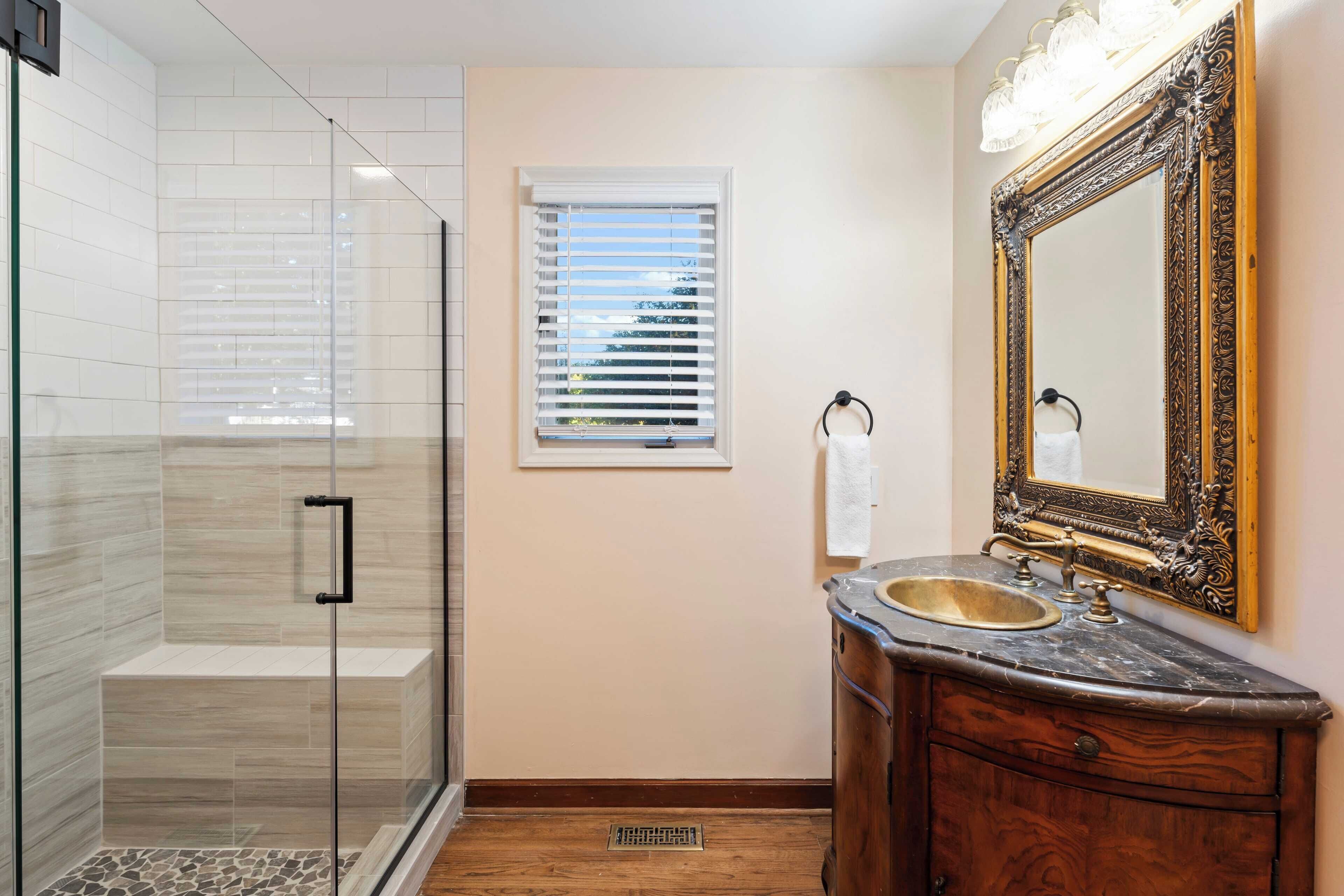 A bathroom with a glass shower enclosure, a vanity with a sink, and a large ornate mirror.