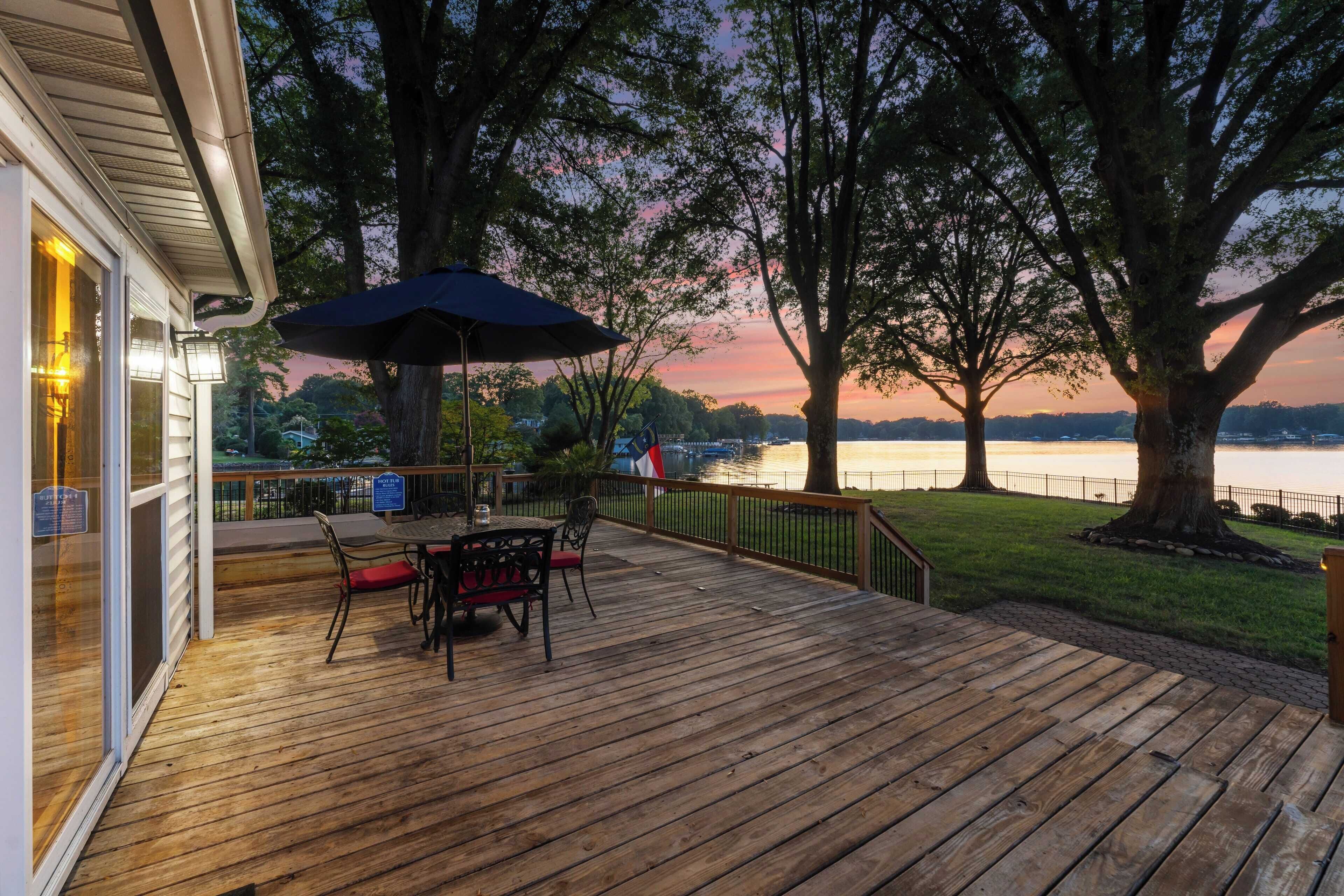 Una terraza de madera con una mesa y sillas, con vistas a un lago al atardecer.