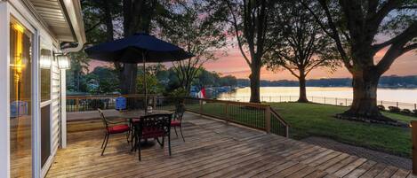 Una terraza de madera con una mesa y sillas, con vistas a un lago al atardecer.