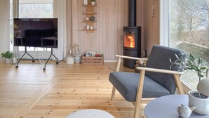 A cozy living room with a fireplace, wooden flooring, a sofa, a TV on a stand, and a view of the outdoors. - Awesome home in Ebeltoft with WiFi (Ebeltoft)