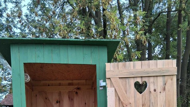 En utetoalett av trä med grön utsida och ett hjärtformat utskuret mönster i dörren.