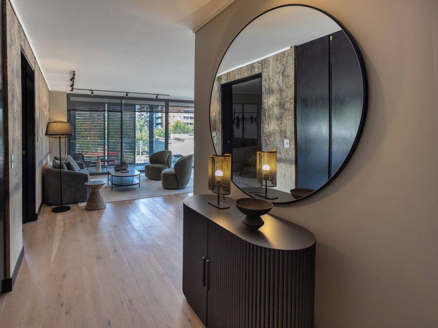Una sala de estar moderna con un espejo redondo grande, un mueble de madera oscura y una zona de estar con sofá y sillones.