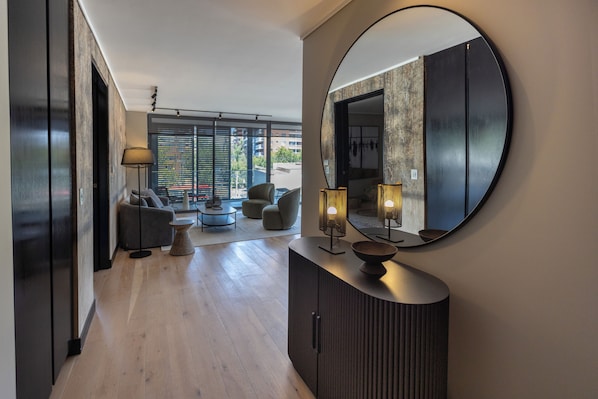 A modern living room with a large round mirror, a dark wooden cabinet, and a seating area with a sofa and armchairs. - AT HOME Alonso (Santiago)