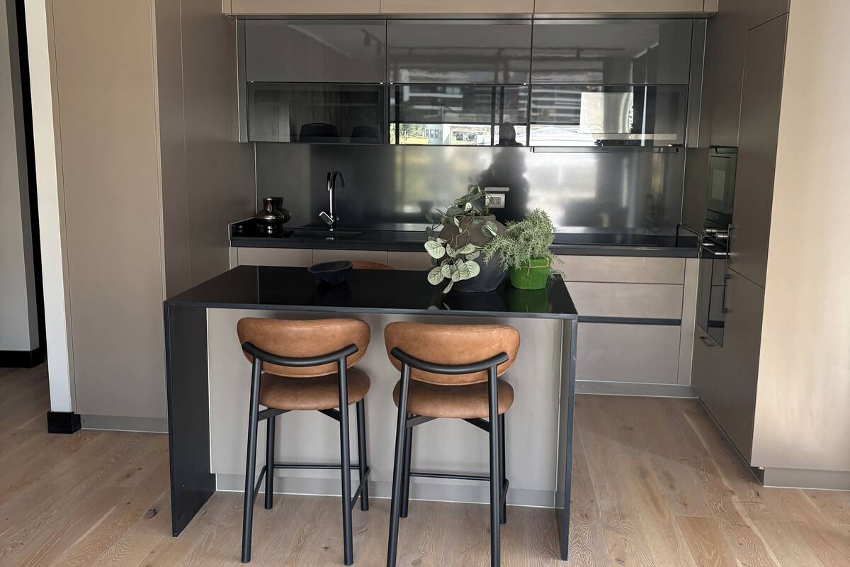 A modern kitchen with a central island, two bar stools, and a potted plant.