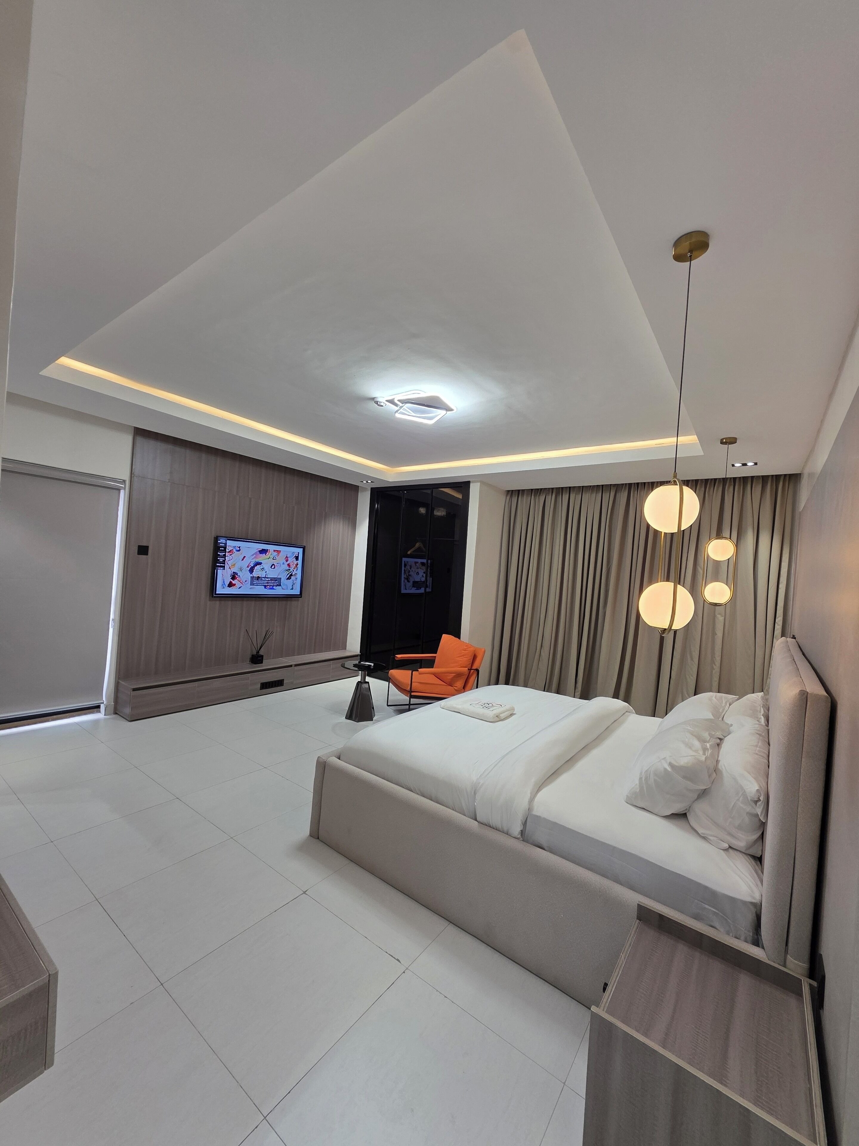 A modern bedroom with a large bed, a TV, and a seating area with a chair.
