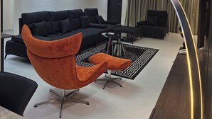 Ein modernes Wohnzimmer mit einem Ecksofa, einem orangefarbenen Sessel, einem Couchtisch und einem Fernseher.