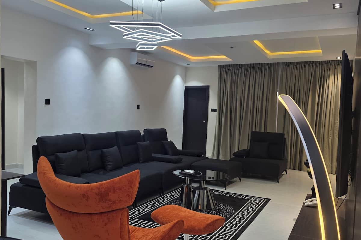 A modern living room with a sectional sofa, an orange chair, a coffee table, and a TV.