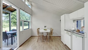 Une cuisine aux murs blancs, une table à manger avec des chaises, et une vue sur l’extérieur grâce à de grandes fenêtres.