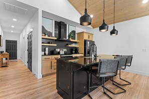 A modern kitchen with a central island, wooden cabinets, and pendant lighting.