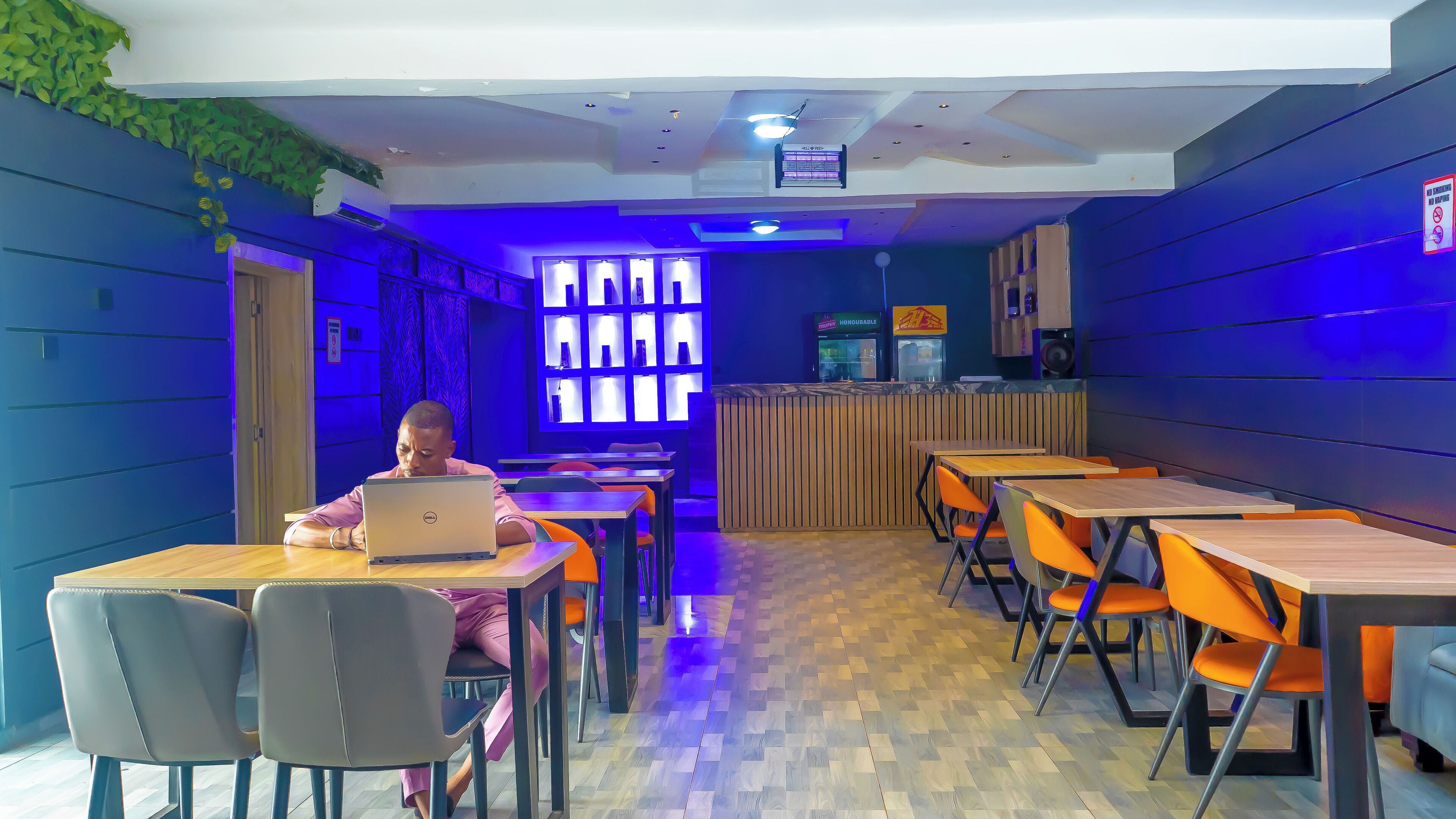 A modern restaurant interior with wooden tables and chairs, a reception desk, and a blue-lit wall.