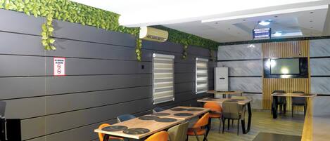 A modern indoor dining area with a long wooden table, orange chairs, and a TV mounted on the wall.