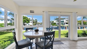 A dining area with a table and chairs, large windows with a view of a swimming pool and greenery, and a 'NO SWIMMING' sign. - Highland Beach Hideaway with Dock (Highland Beach)