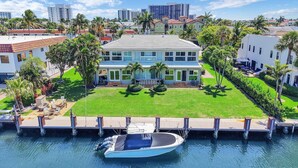 A two-story house with a dock and a boat, surrounded by palm trees and a clear sky. - Highland Beach Hideaway with Dock (Highland Beach)