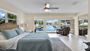A bedroom with a bed, a ceiling fan, a view of a pool and palm trees, and a sliding glass door leading to a balcony. - Highland Beach Hideaway with Dock (Highland Beach)