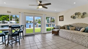A spacious living area with a ceiling fan, a dining table with chairs, a sofa, and large windows offering a view of a pool and palm trees. - Highland Beach Hideaway with Dock (Highland Beach)